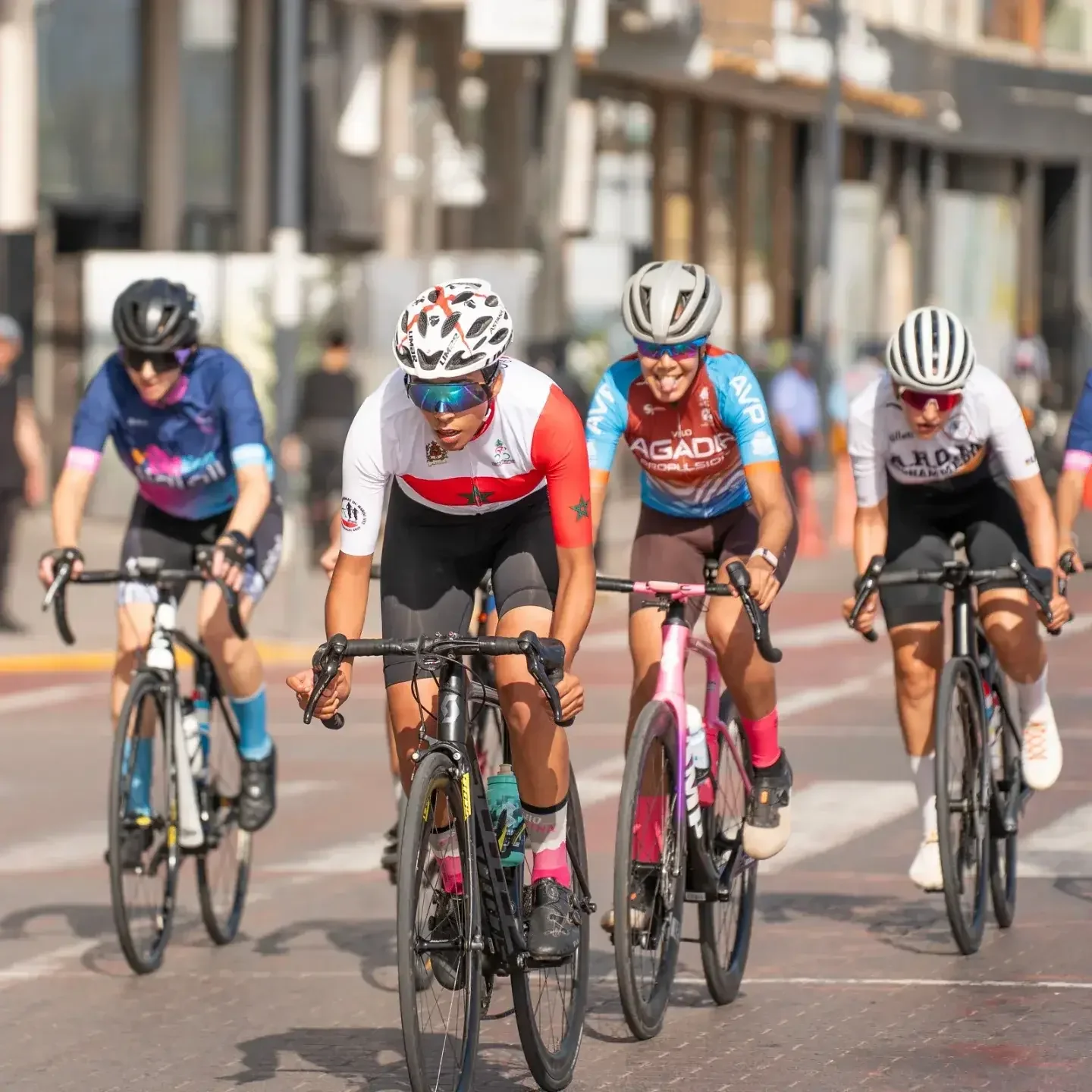 Women road cyclists racing through a city street, led by the Moroccan national champion