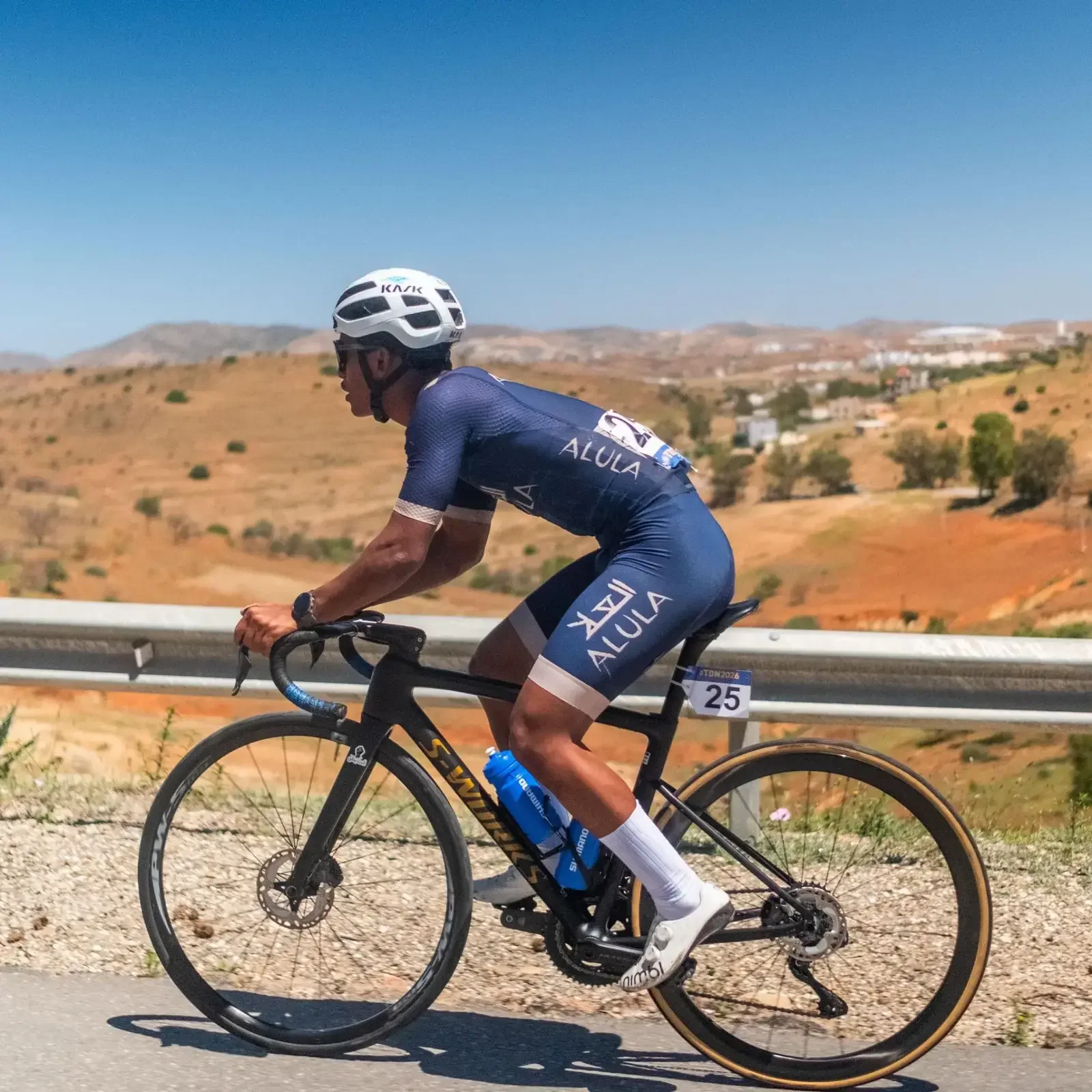 AlUla team cyclist riding through a dry hillside landscape